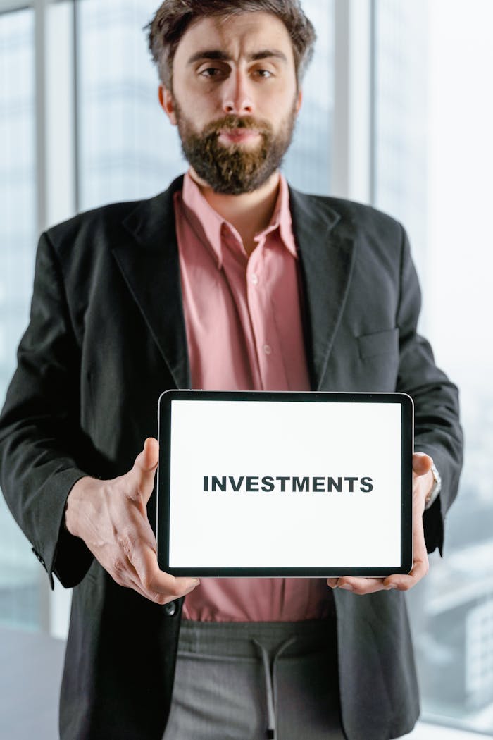 Businessman holding tablet displaying the word 'Investments' in an office setting.